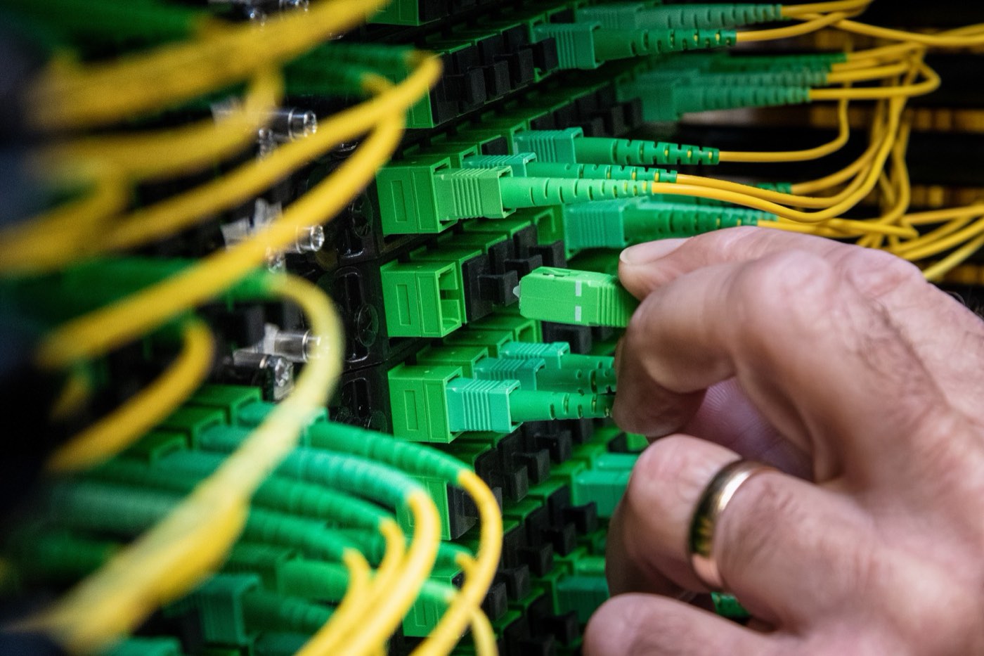 Hands connecting fibre-optic cables in a network rack